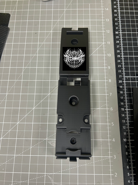Close-up of a gray 3D-printed functional component with detailed geometry and mounting features, photographed on a textured black surface.