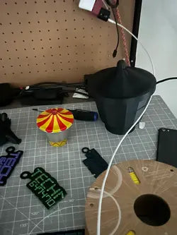 Workspace with 3D-printed movie model, featuring the original colorful tent-like part provided by the customer and the scaled-up black cone-shaped model printed for movie production using high-precision scanning and 3D printing technology.