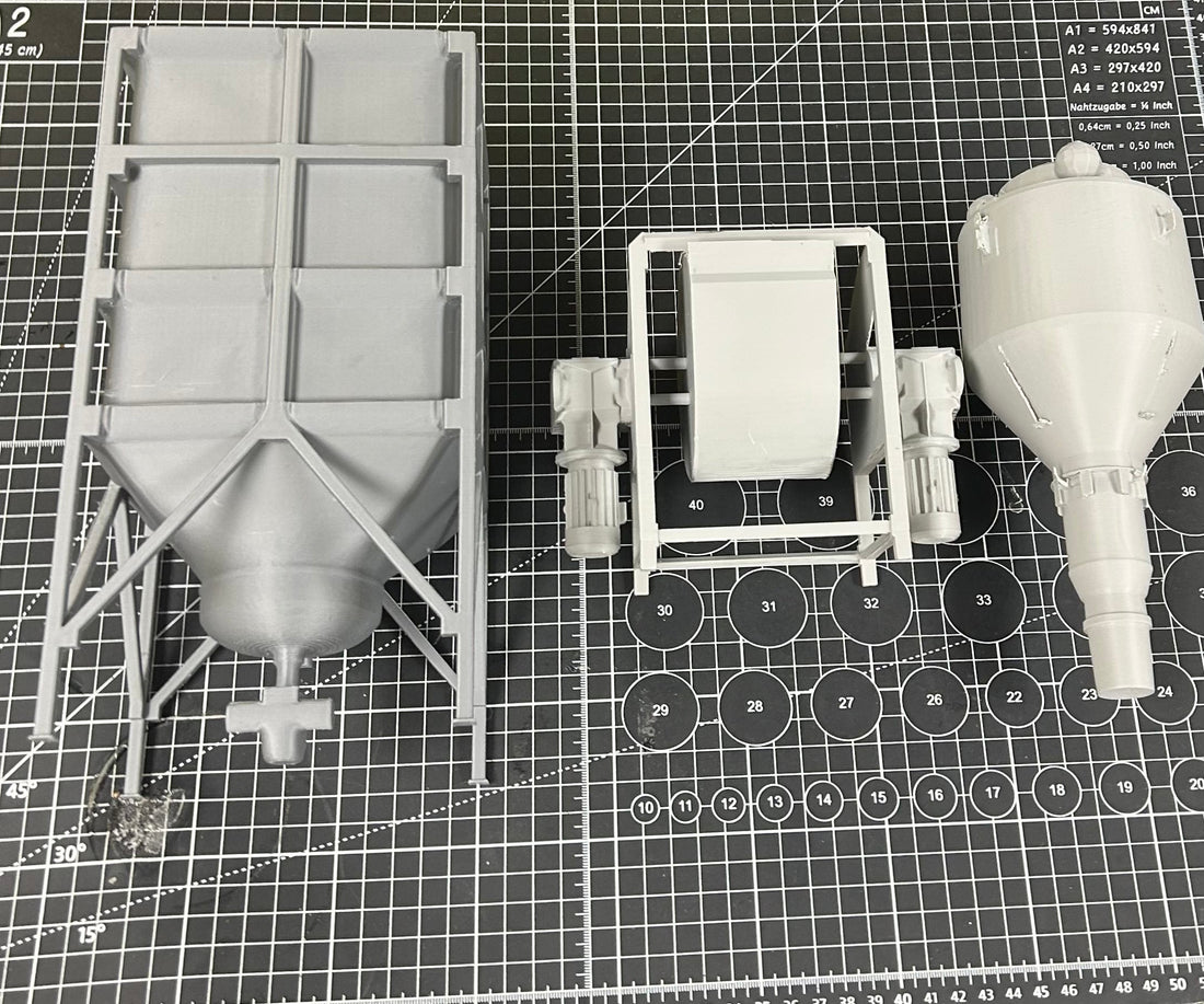 Top-down view of three large, gray 3D-printed industrial components on a measurement grid cutting mat, showcasing detail and scale. Parts include a mixer, a hopper, and a cyclone separator.