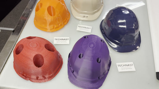 Dense red, orange and purple TECHNAST hard-hat production jigs displayed beside beige and blue hard-hat shells