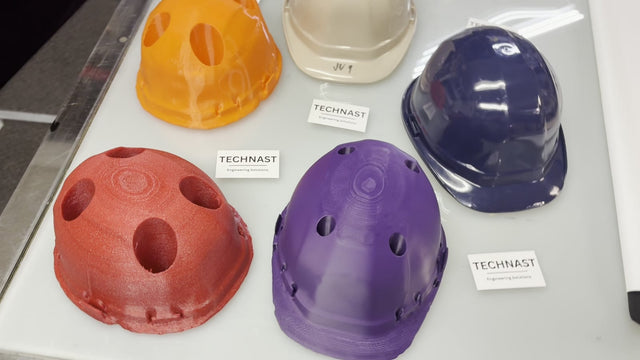 Dense red, orange and purple TECHNAST hard-hat production jigs displayed beside beige and blue hard-hat shells